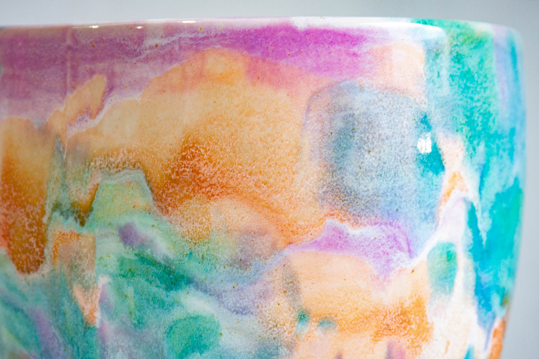 Close-up of a ceramic bowl with a colorful marbled glaze featuring orange, purple, teal, and white.