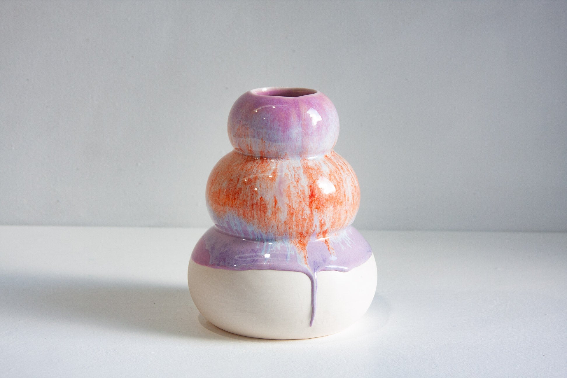A small ceramic vase with a three-tiered stacked design, featuring a glossy purple and orange marbled glaze on the upper tiers and a matte white base with a purple drip.