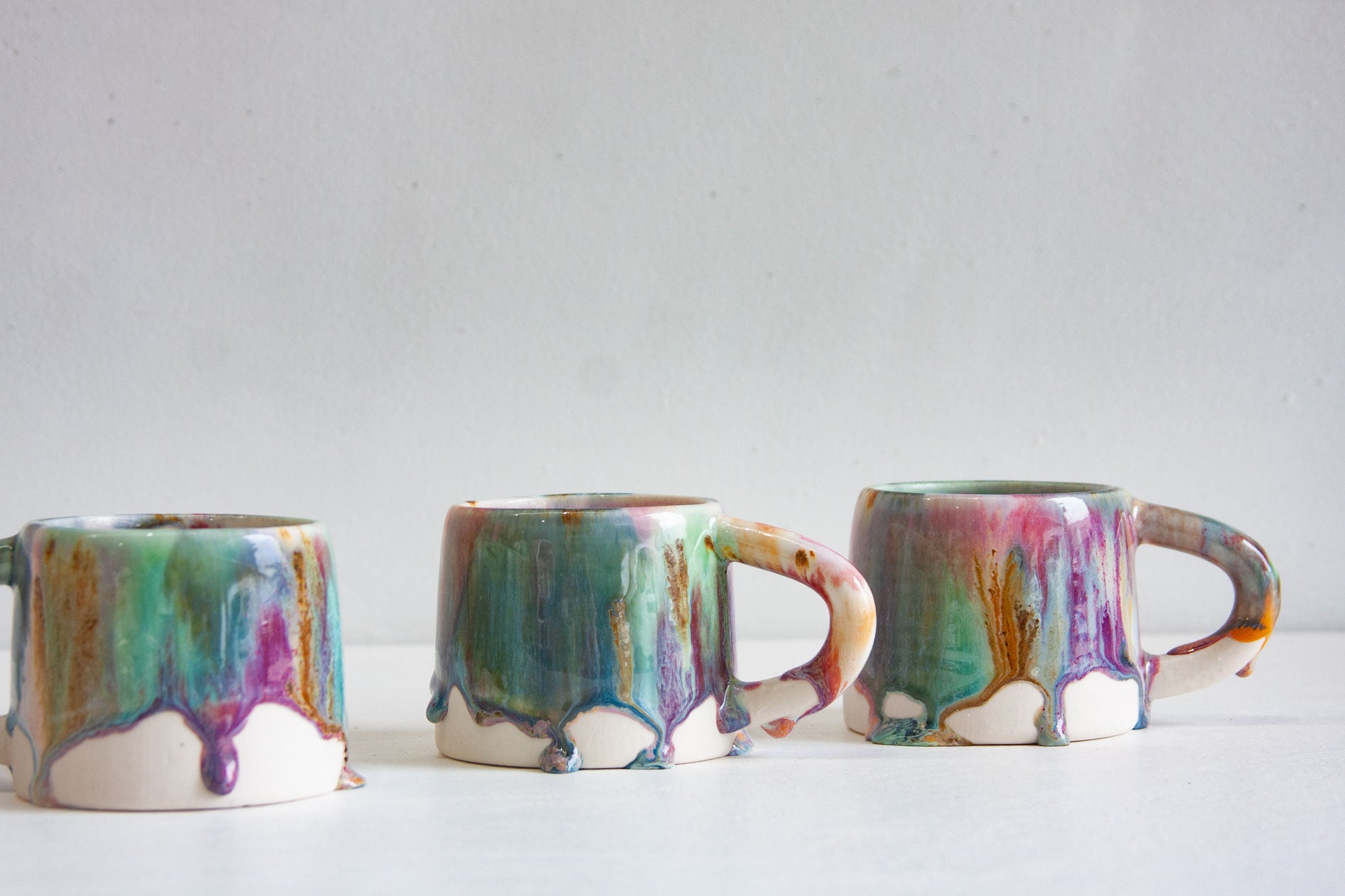 Three handmade ceramic mugs grouped together, each with the Bottlebrush glaze running in long vertical drips over a bare white clay base.