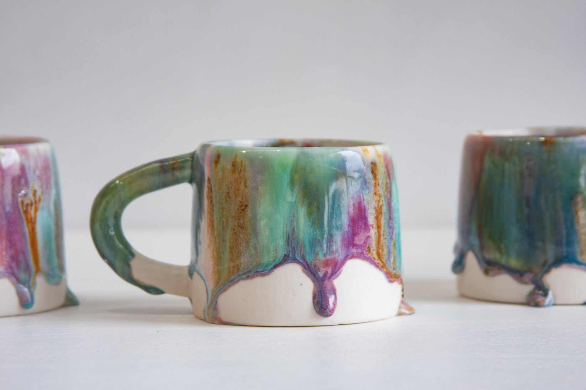 Close-up of a handmade ceramic mug, the green, pink and brown glaze gathering into a heavy bead that hangs below the glaze line.