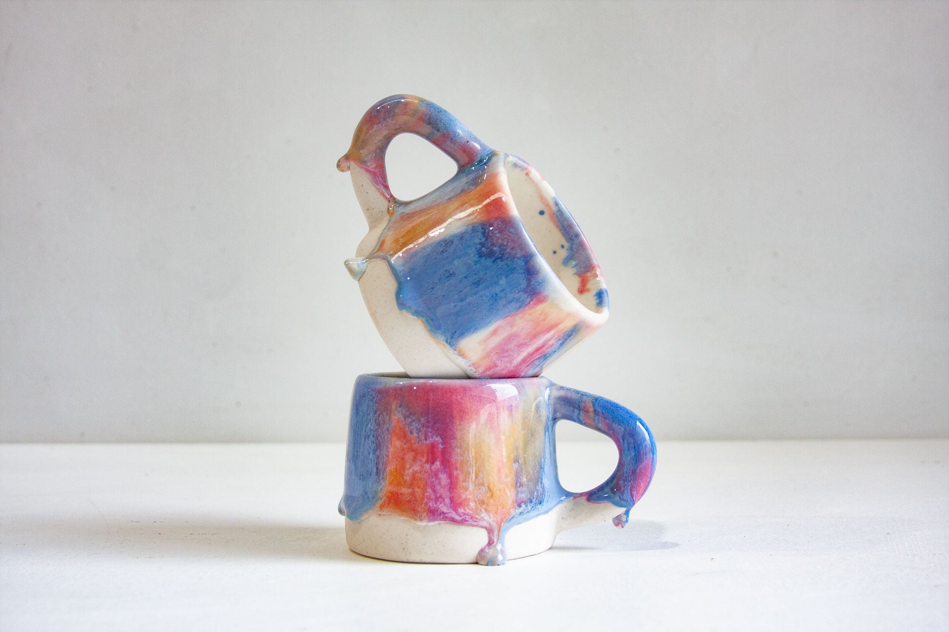 two handmade ceramic mugs one on top of the other sitting on a table