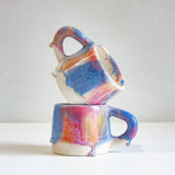 two handmade ceramic mugs one on top of the other sitting on a table