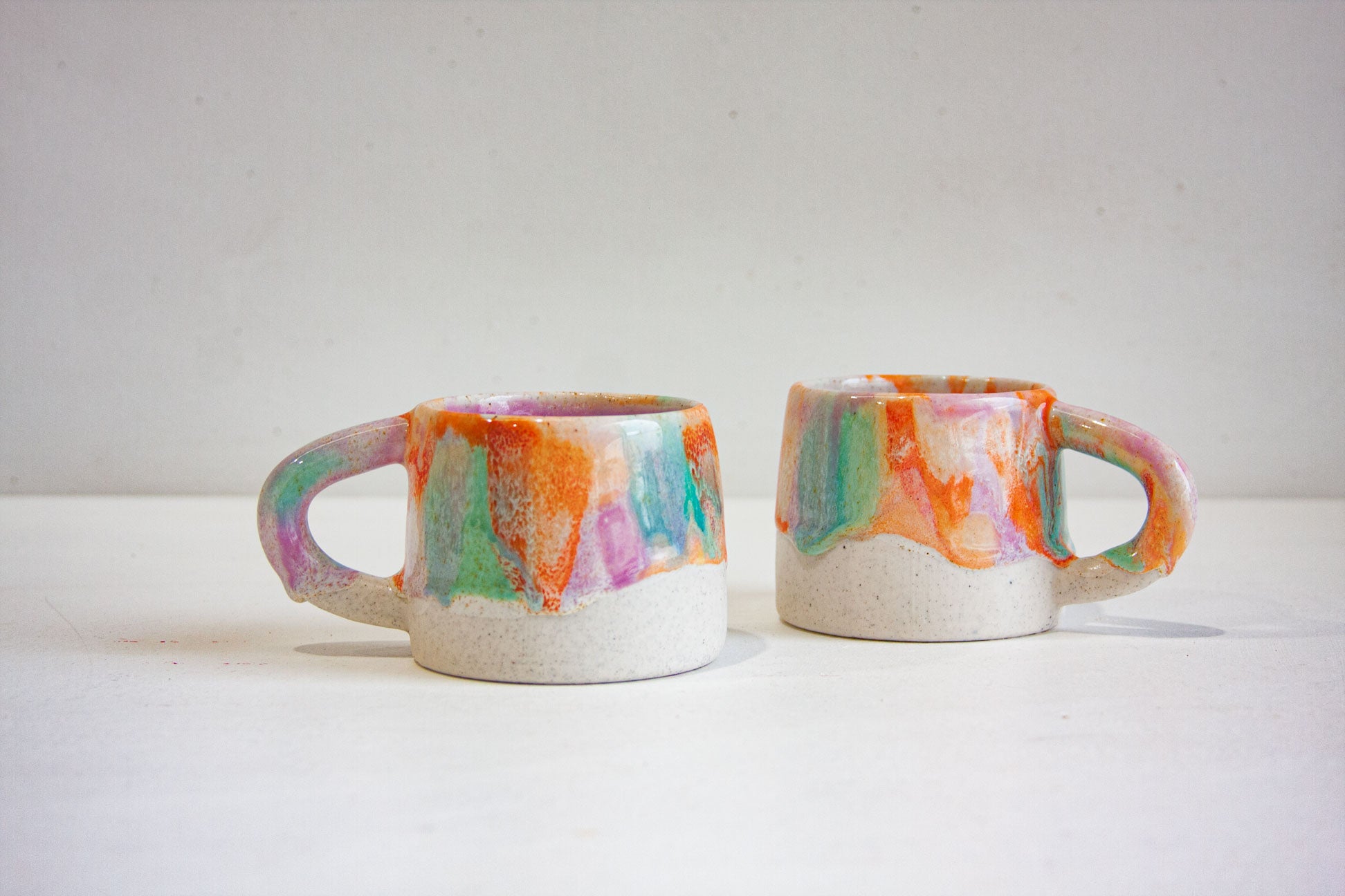 photo of two handmade ceramic mugs glazed in purple, green and orange mug 