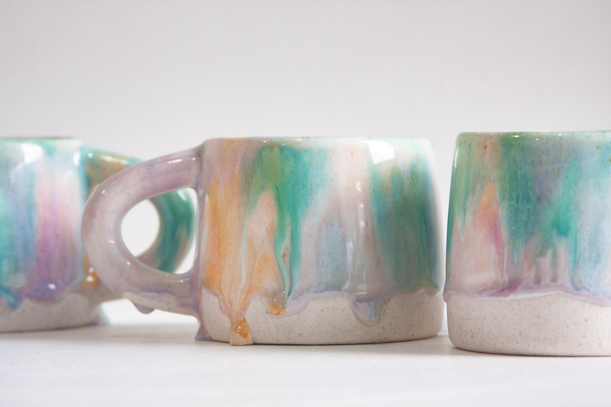 Three ceramic mugs with multicolored marbled design on a white background