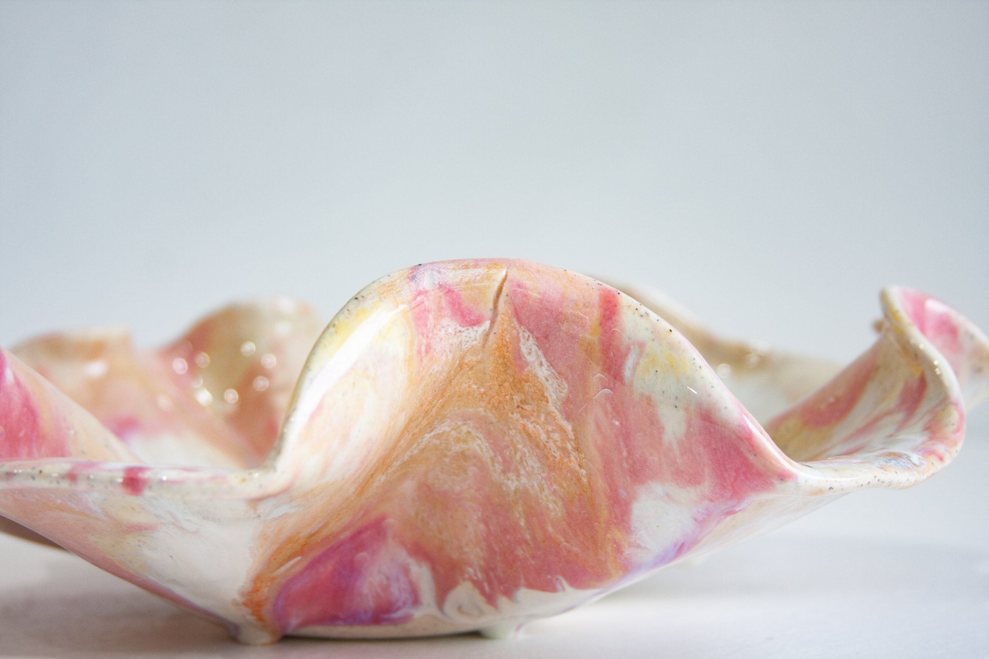 Close-up of one raised fold of a handmade ceramic oyster platter, showing a fine superficial crack that has filled with glaze, running down from the rim.