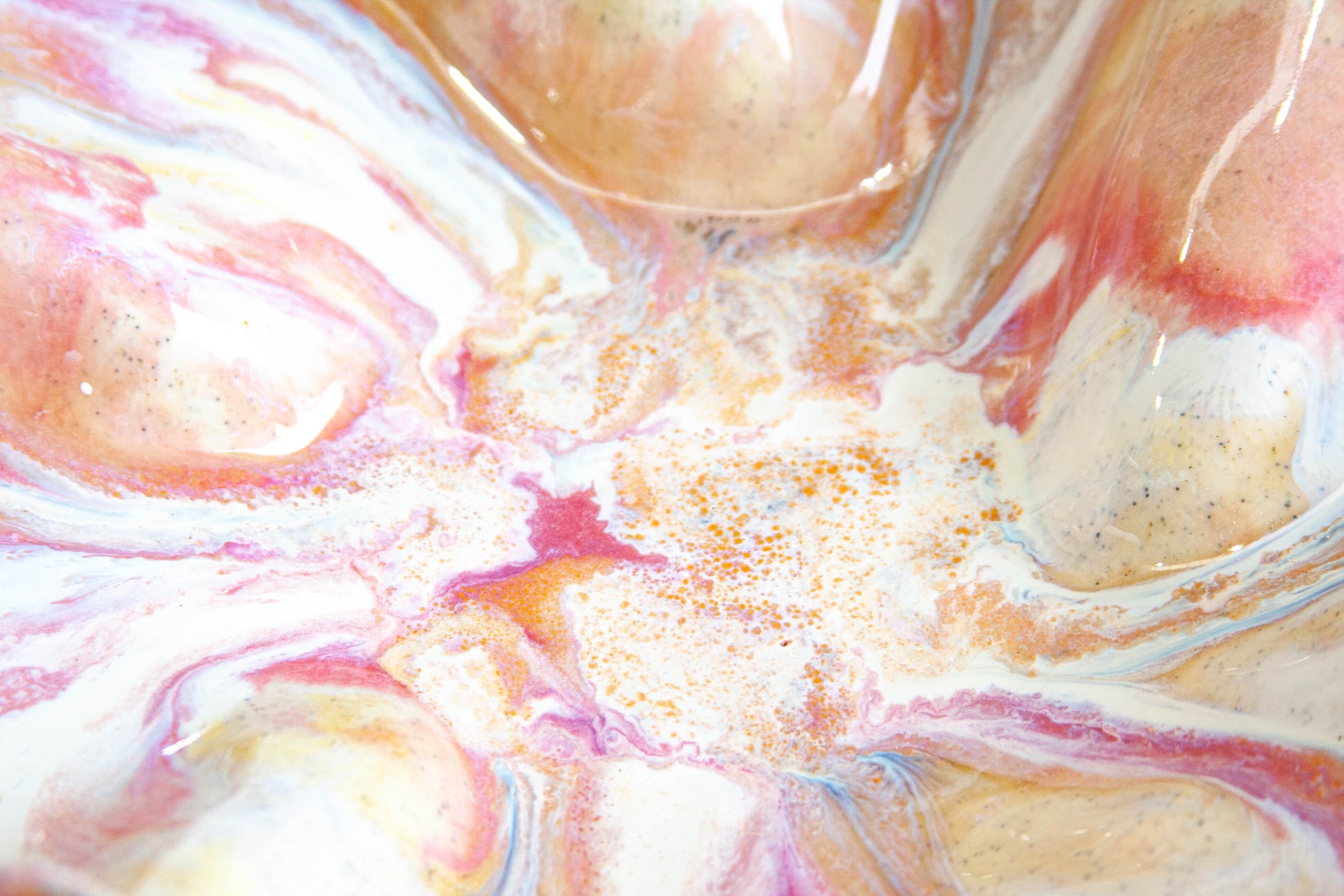 Macro view of the glaze on a handmade ceramic oyster platter, marbled pink, peach and cream with fine orange speckles pooling toward the centre.