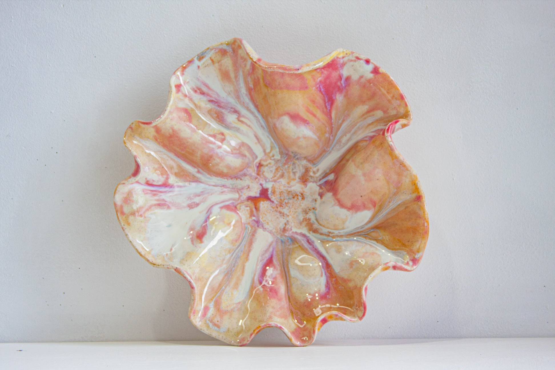 A handmade ceramic oyster platter seen from above, the folded rim forming a shell-like shape, glazed in pink, peach and cream over speckled clay.