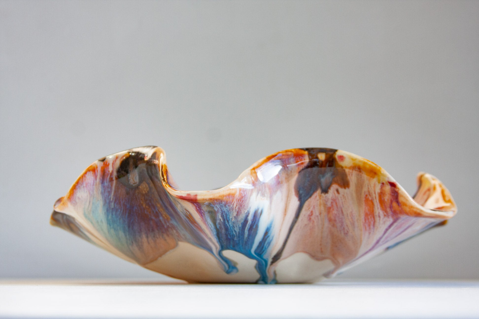 handmade ceramic oyster shaped platter glazed in blue, brown, peach and pink.