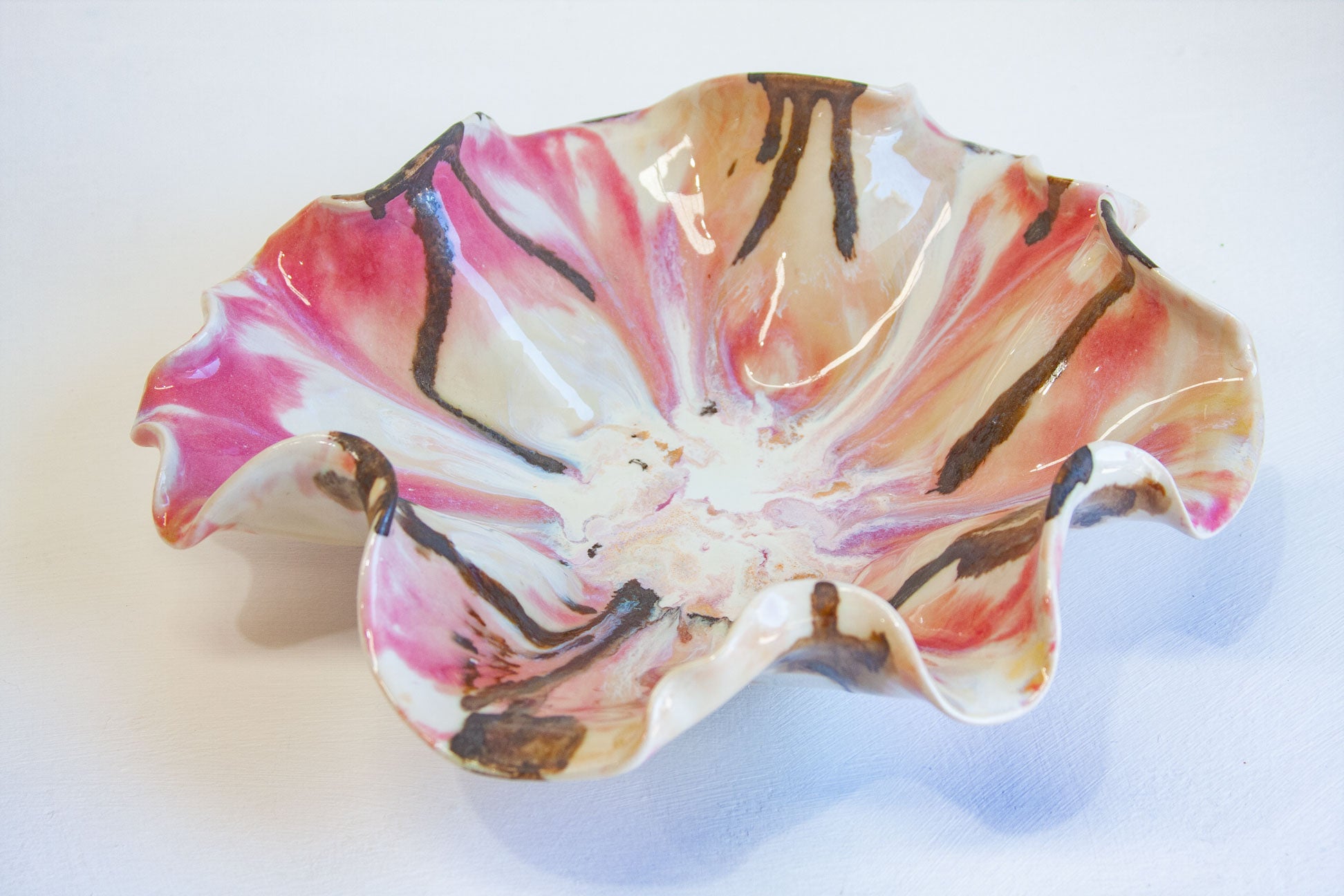 A handmade ceramic flower-shaped bowl with a glossy finish, featuring pink, peach, and brown marbled patterns on a white base, set against a plain white background.