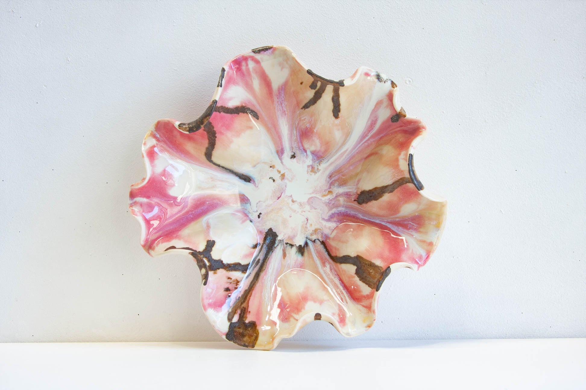 A handmade ceramic flower-shaped bowl with a glossy finish, featuring pink, white, and brown marbled patterns, set against a plain white background.