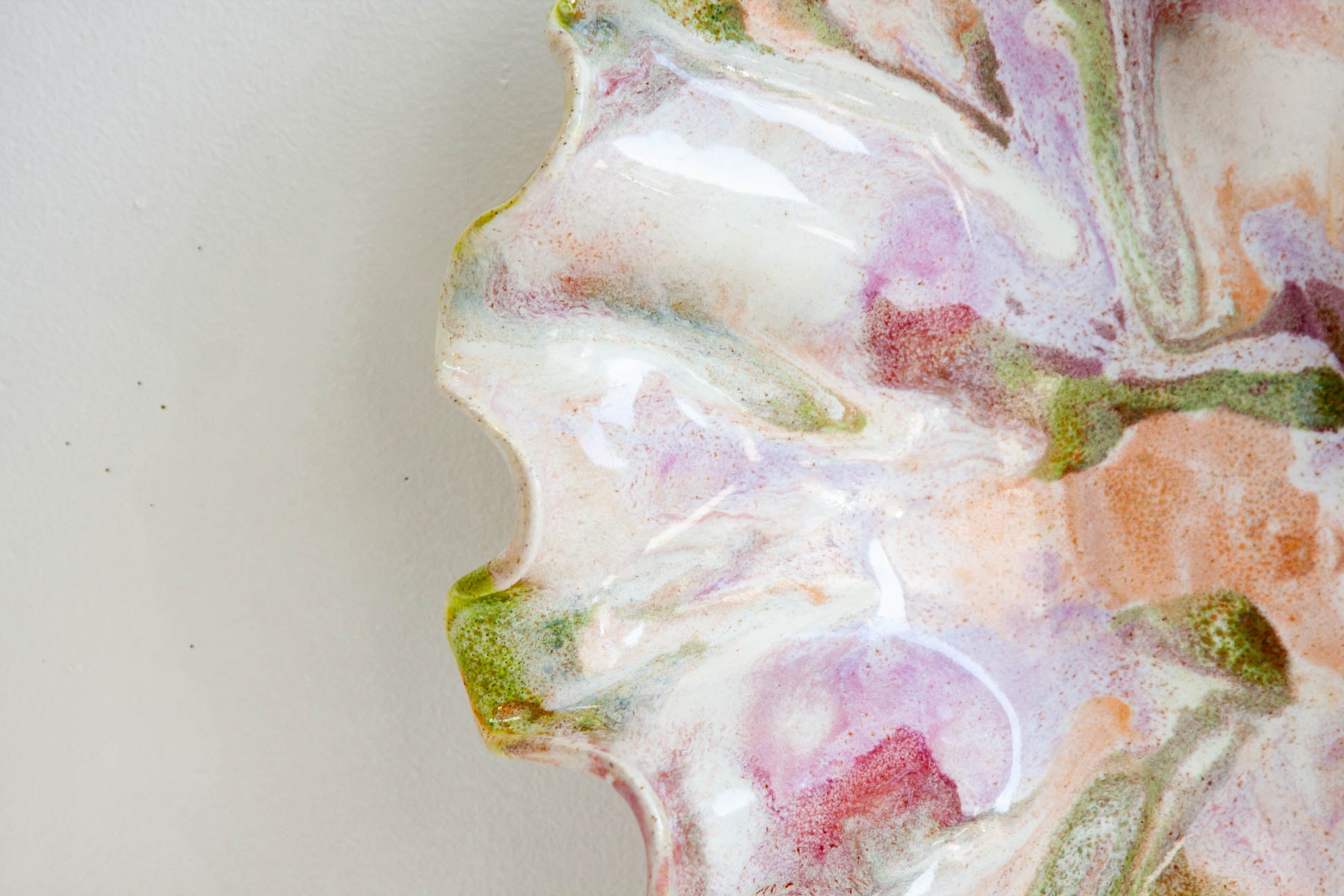 A close-up of a handcrafted resin tray with a wavy, organic edge, featuring a marbled pattern of white, pink, purple, green, and peach swirls on a light gray background.