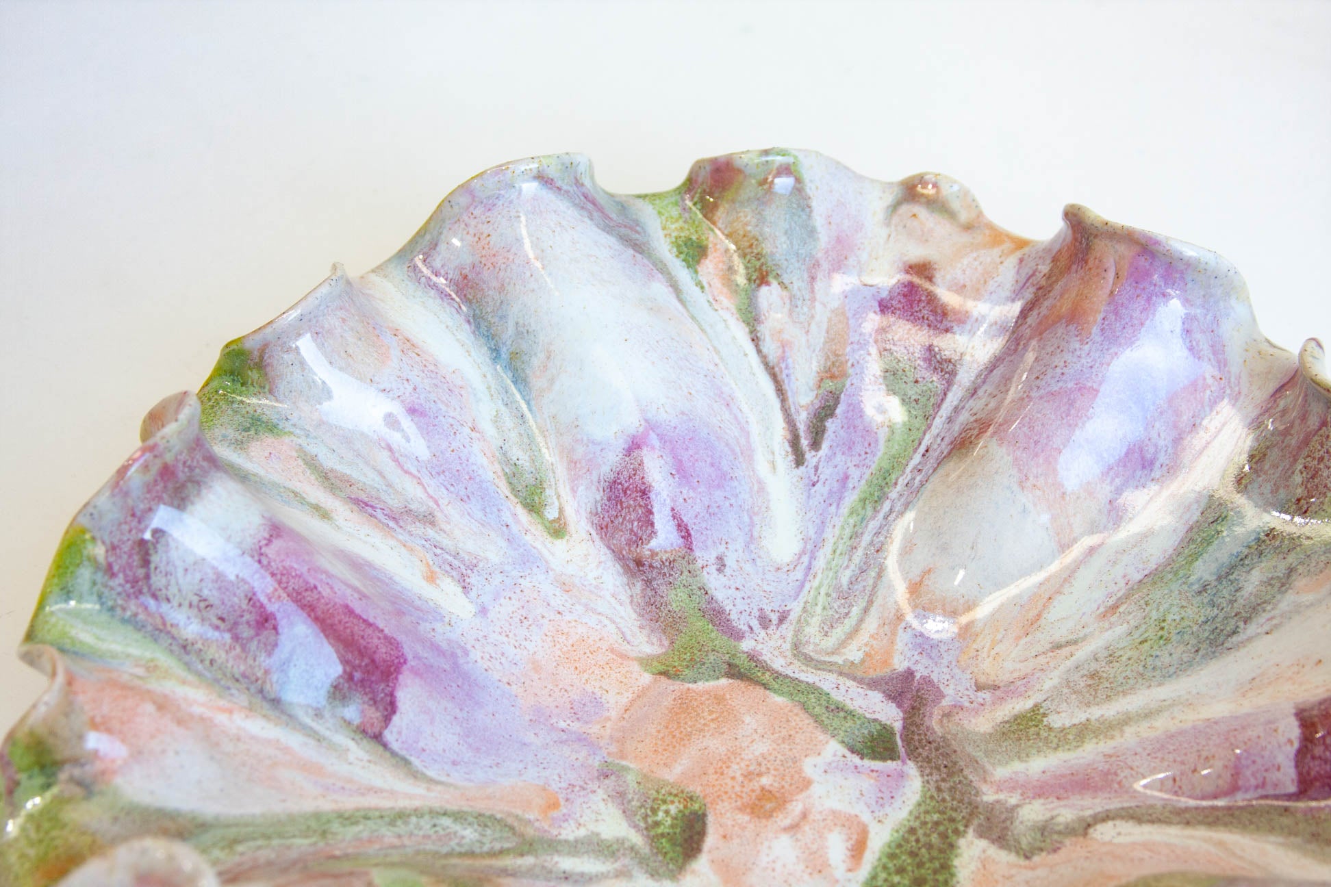 A close-up of a decorative ceramic plate with a ruffled, scalloped edge and a glossy marbled glaze in pastel purple, pink, peach, green, and white.
