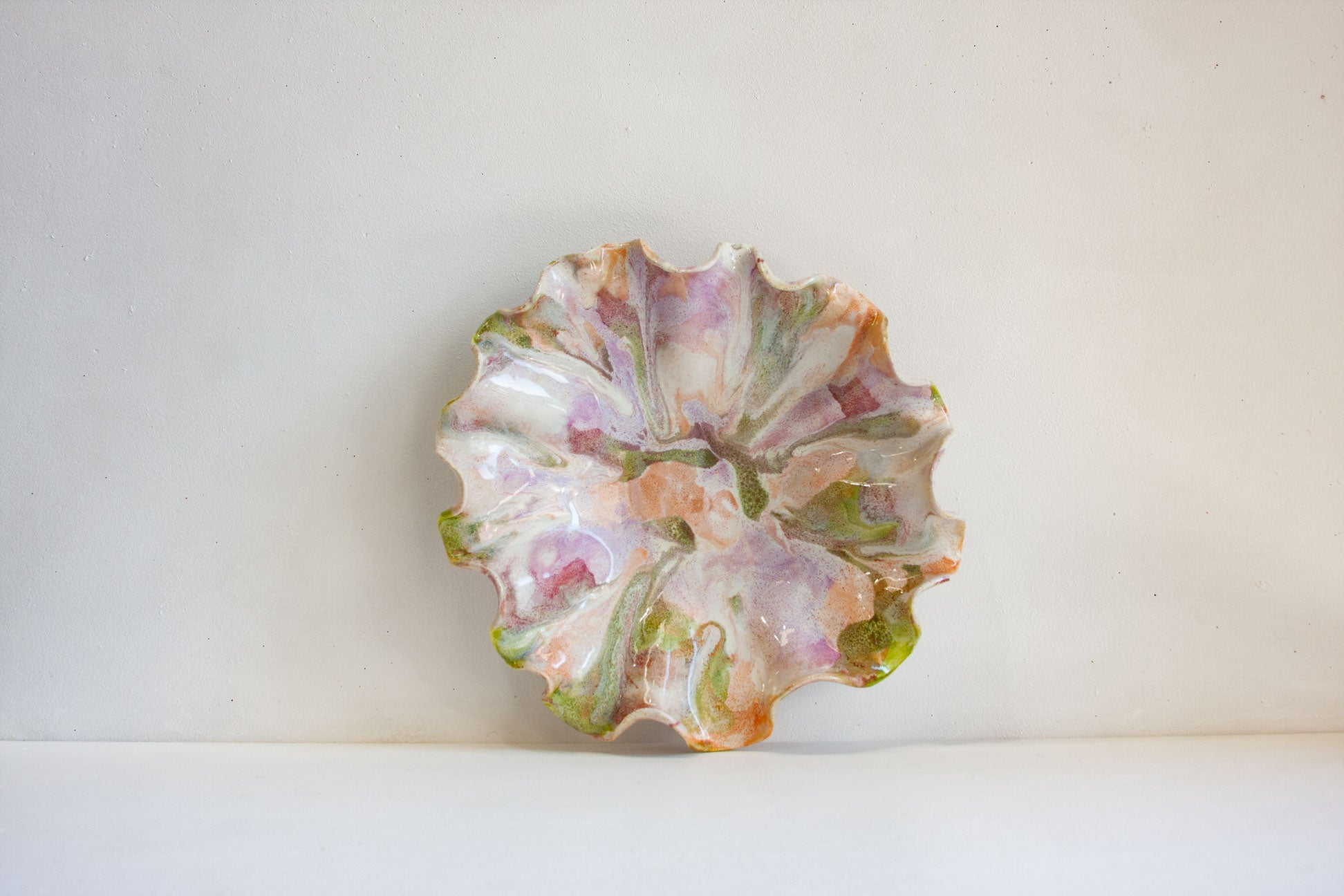 A vintage ceramic flower-shaped bowl with a scalloped rim, decorated with a marbled pattern of pink, green, and orange on an off-white base, set against a plain light background.