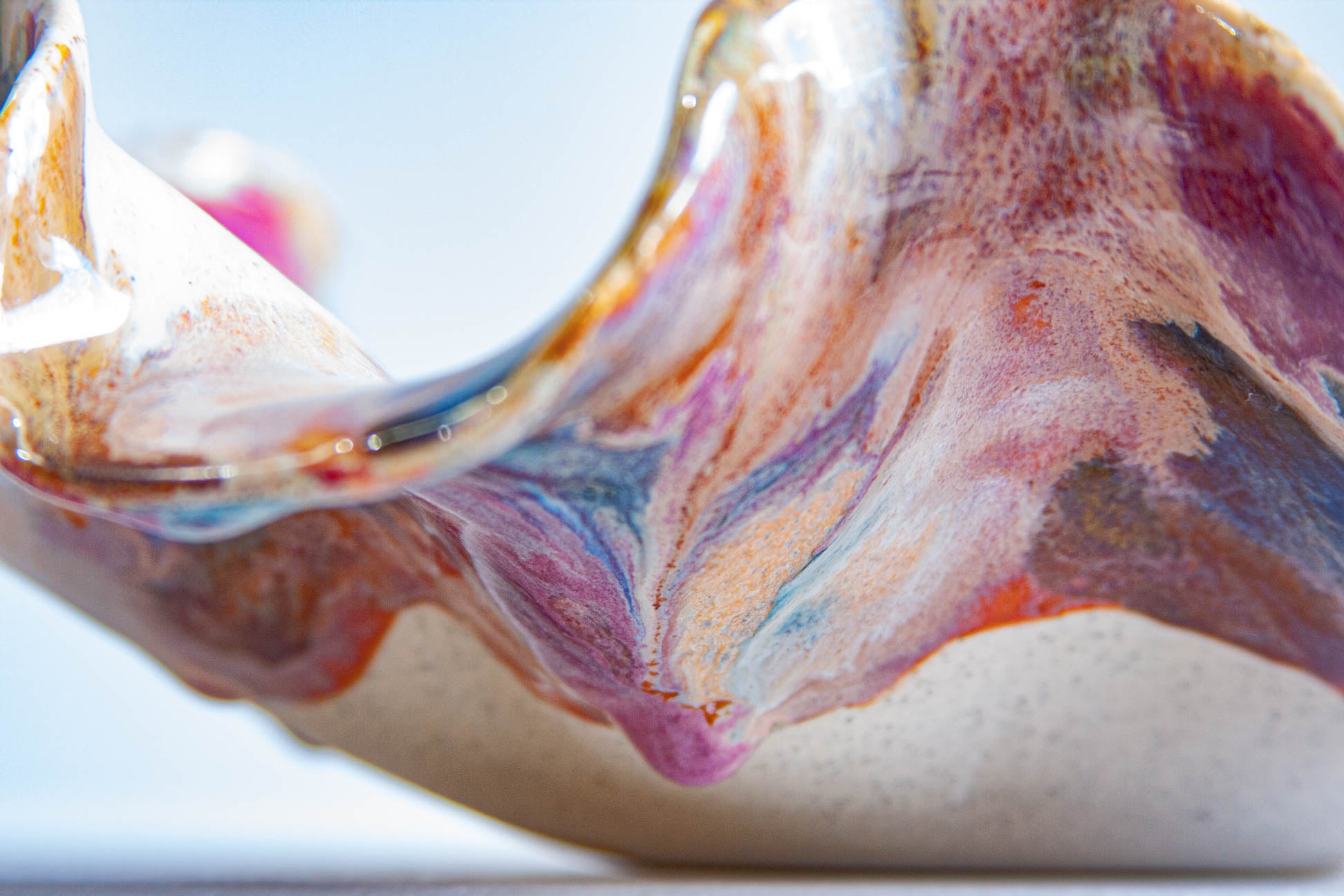 Close-up of a handcrafted ceramic bowl with a wavy rim, featuring a marbled glaze in pink, purple, blue, orange, and white on a speckled beige base.
