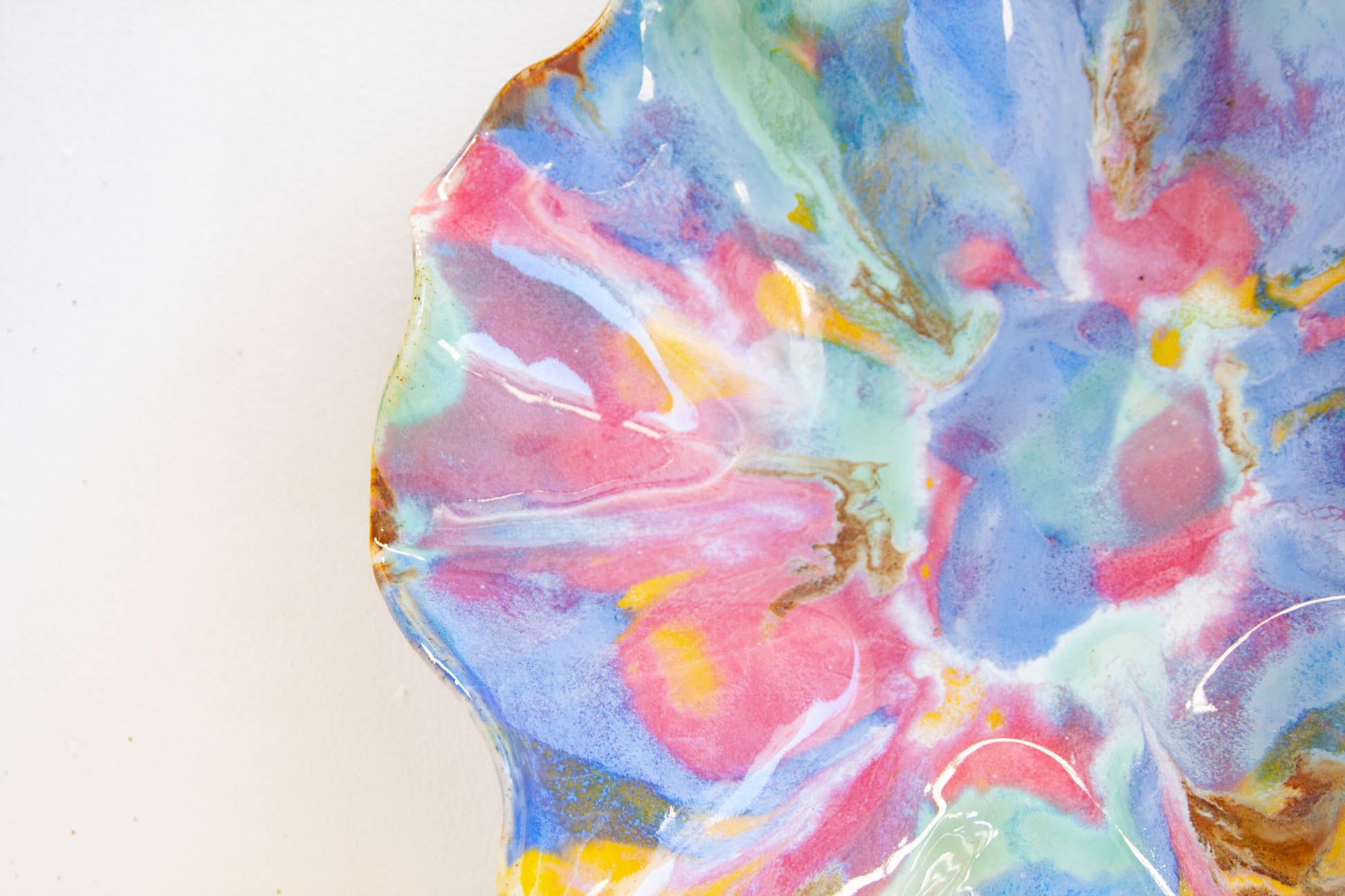 A close-up of a colorful abstract marbled surface with swirling pink, blue, white, mint green, and gold tones on a plain light background.