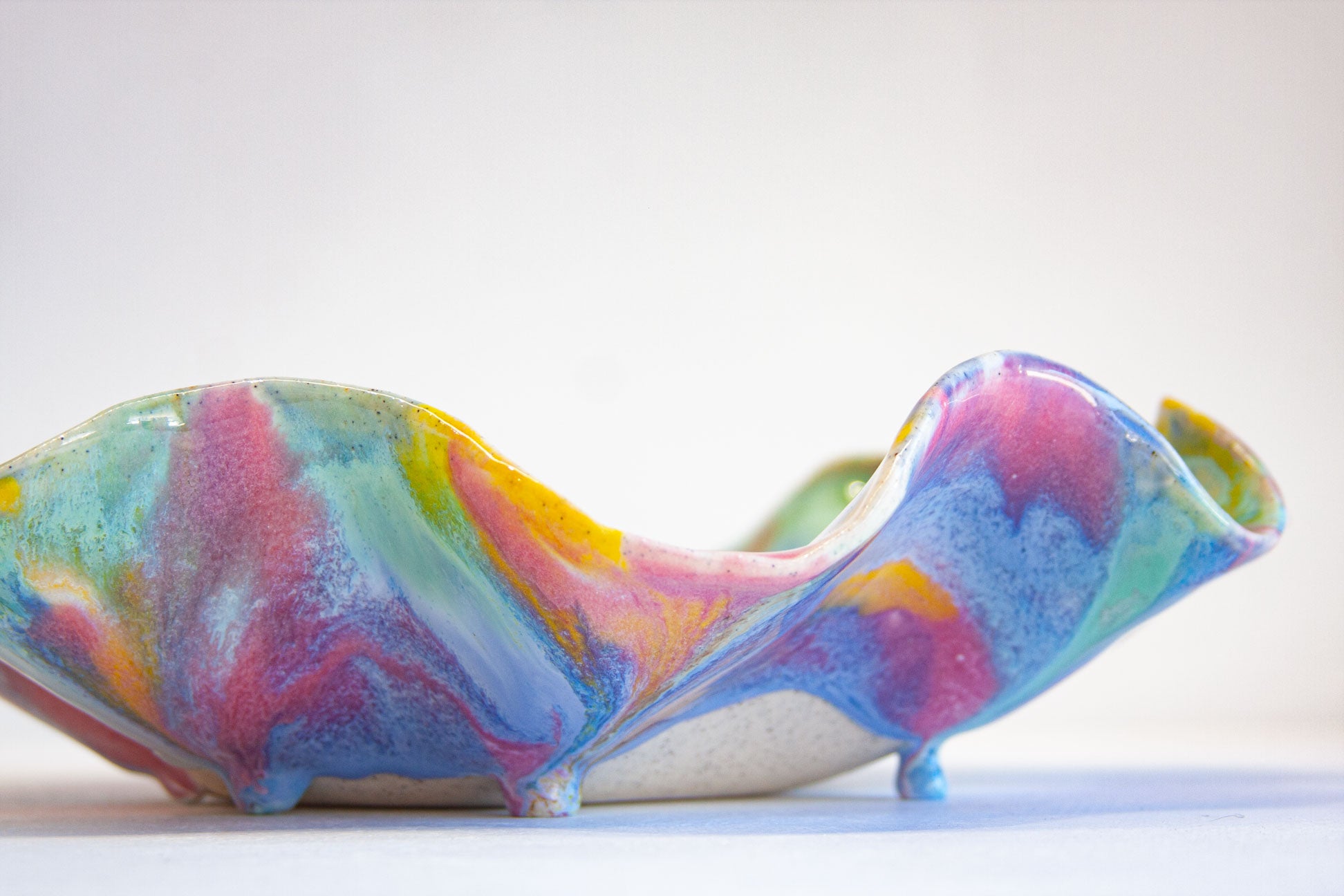 A colorful, organic-shaped ceramic planter with a glossy, marbled glaze in shades of blue, pink, yellow, and green, standing on small feet against a plain white background.