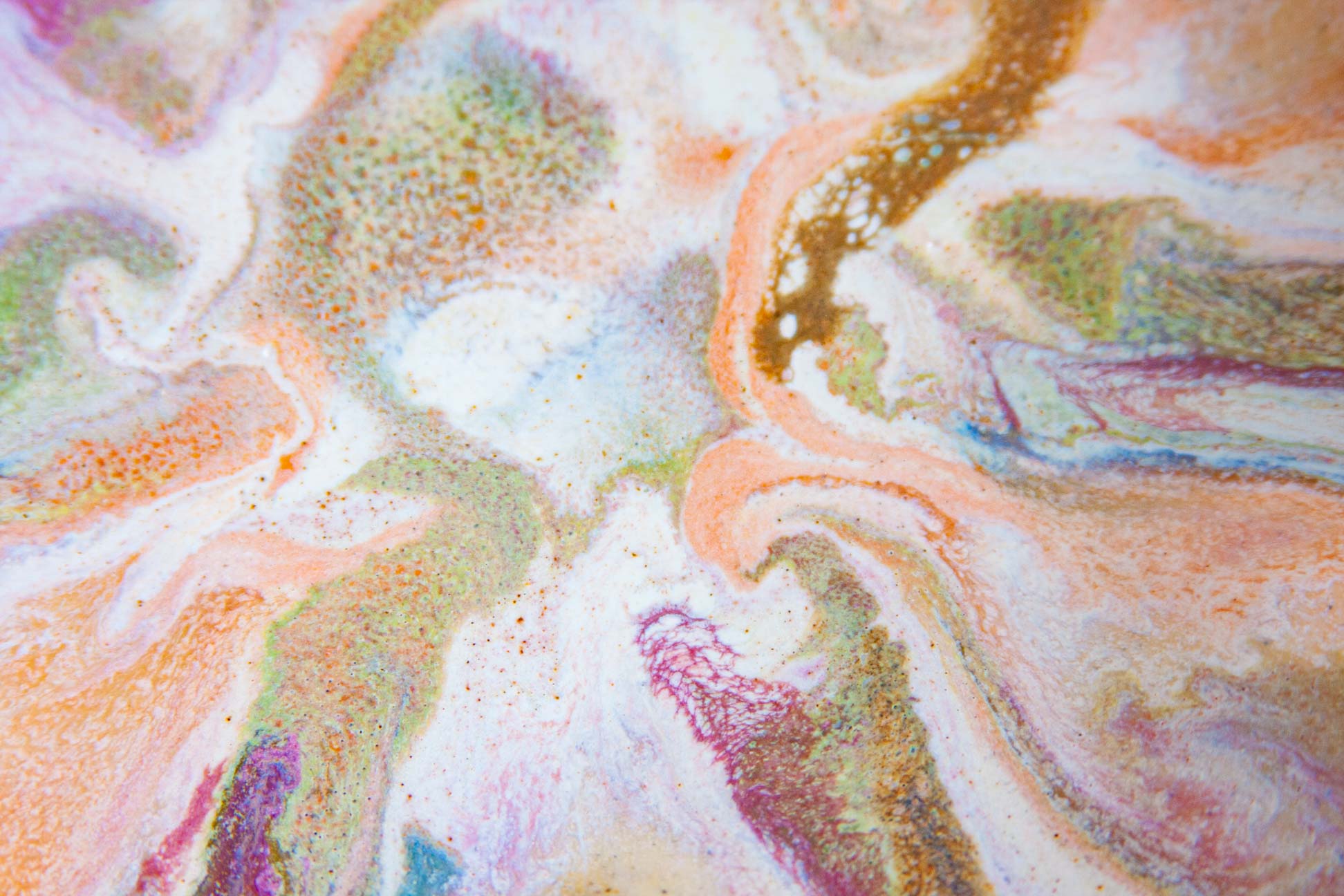 Abstract marbled pattern with swirling pastel orange, pink, purple, green, and white fluid-like textures, plus small gold speckles.