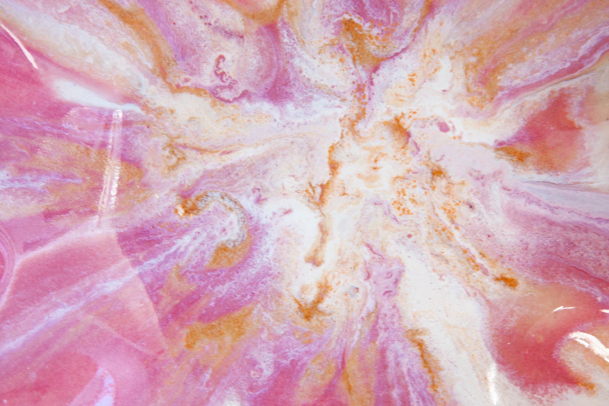 A close-up of a pink, white, and metallic gold marbled or swirled surface with glossy highlights, filling the entire frame.