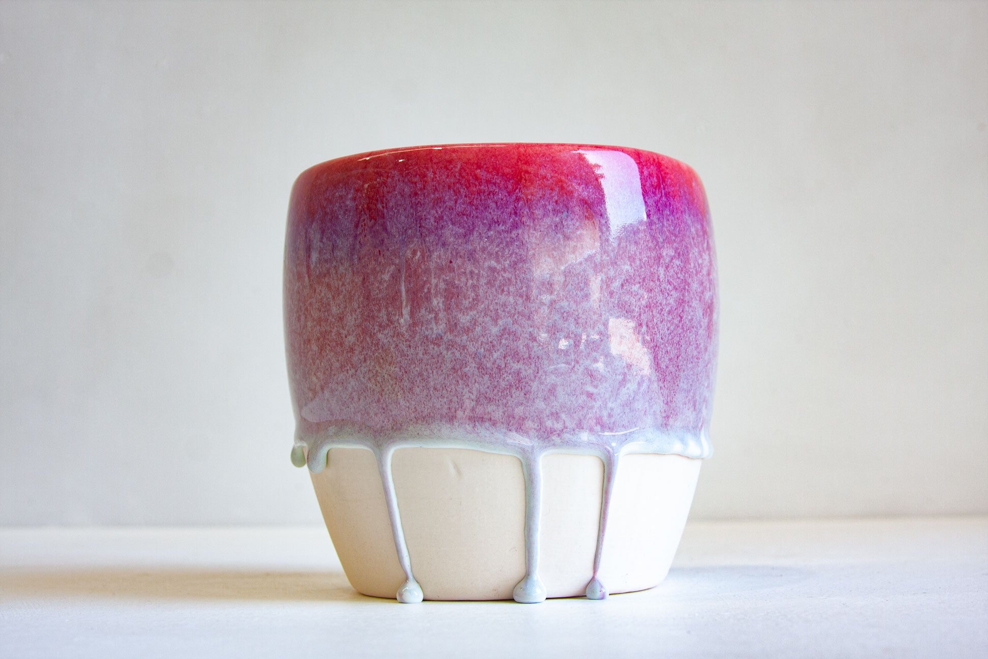 A ceramic planter or vase with a glossy red and purple gradient upper body and a dripping white ceramic base, set against a plain light background.