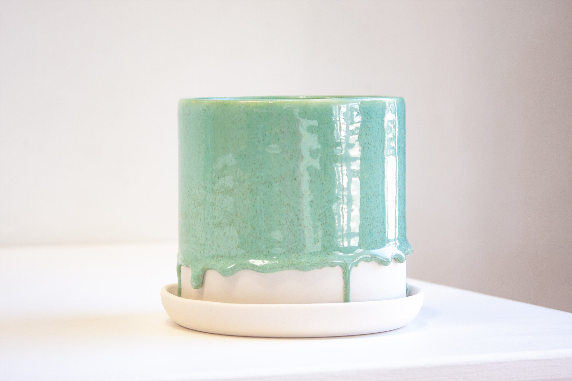 handmade ceramic green glaze planter sits on a unglazed ceramic saucer.