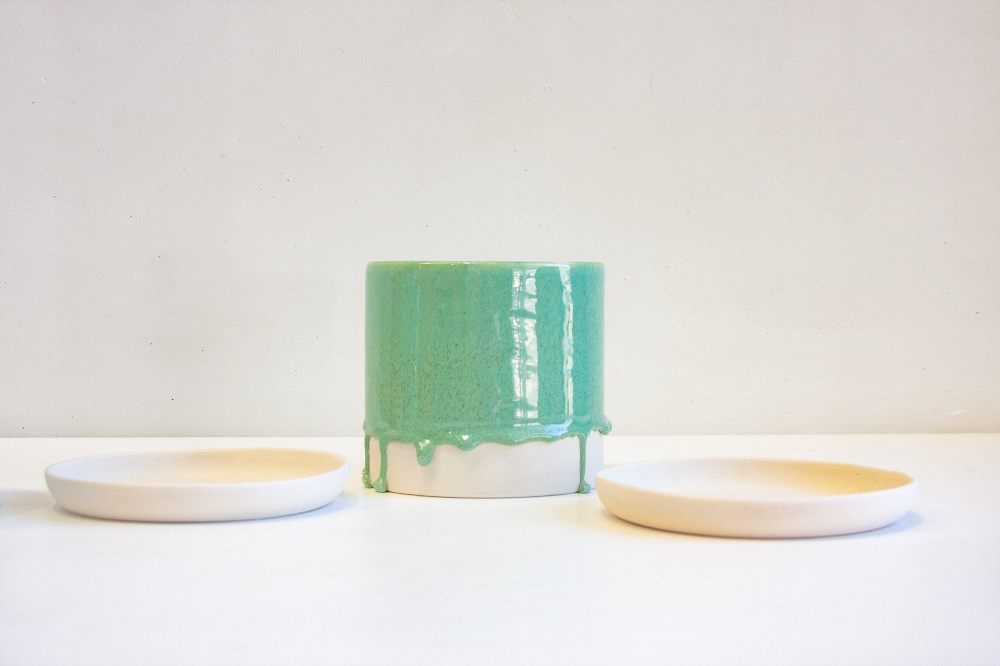 A green ceramic planter sits in between two unglazed ceramic saucers.