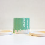 A green ceramic planter sits in between two unglazed ceramic saucers.