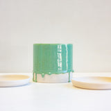 A green ceramic planter sits in between two unglazed ceramic saucers.
