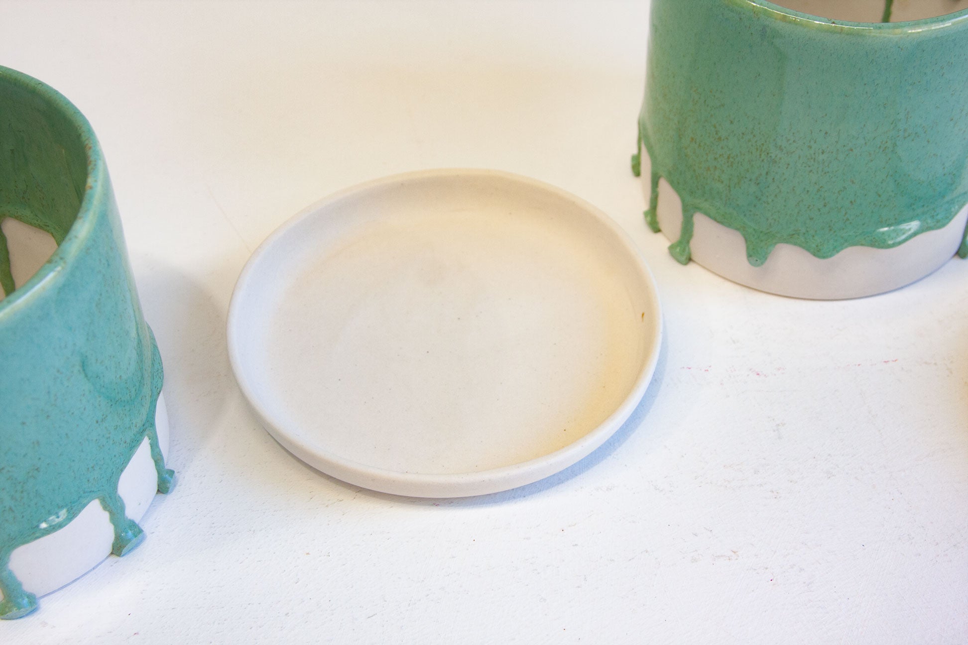 two drippy glazed green planters beside one unglazed ceramic drip tray.