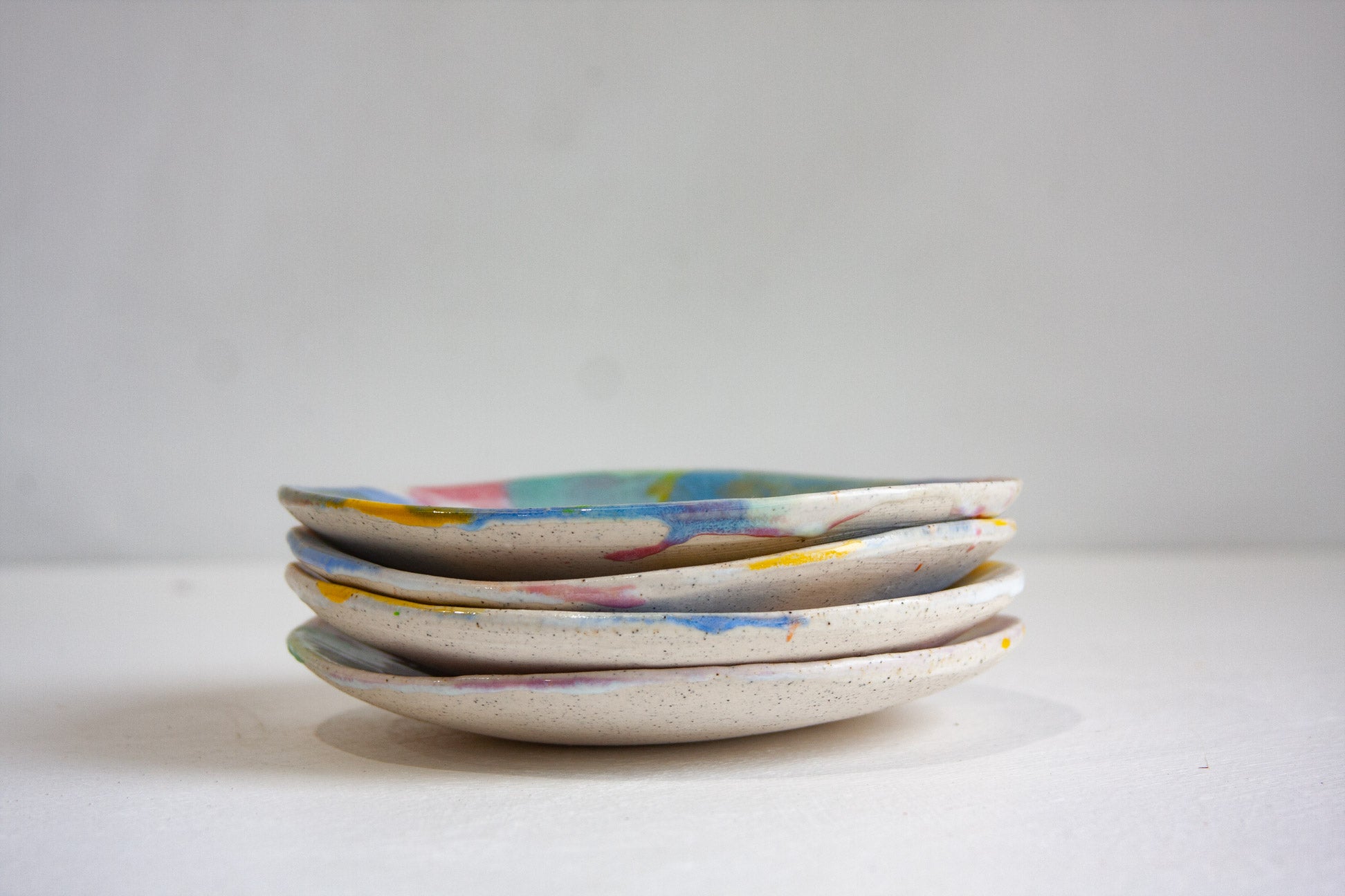 Four handmade ceramic small plates stacked and seen from the side, showing the speckled clay rims and the glaze running over the edges.