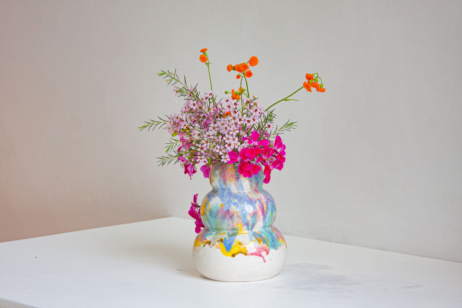 Colorful vase with flowers on a white surface and light gray background