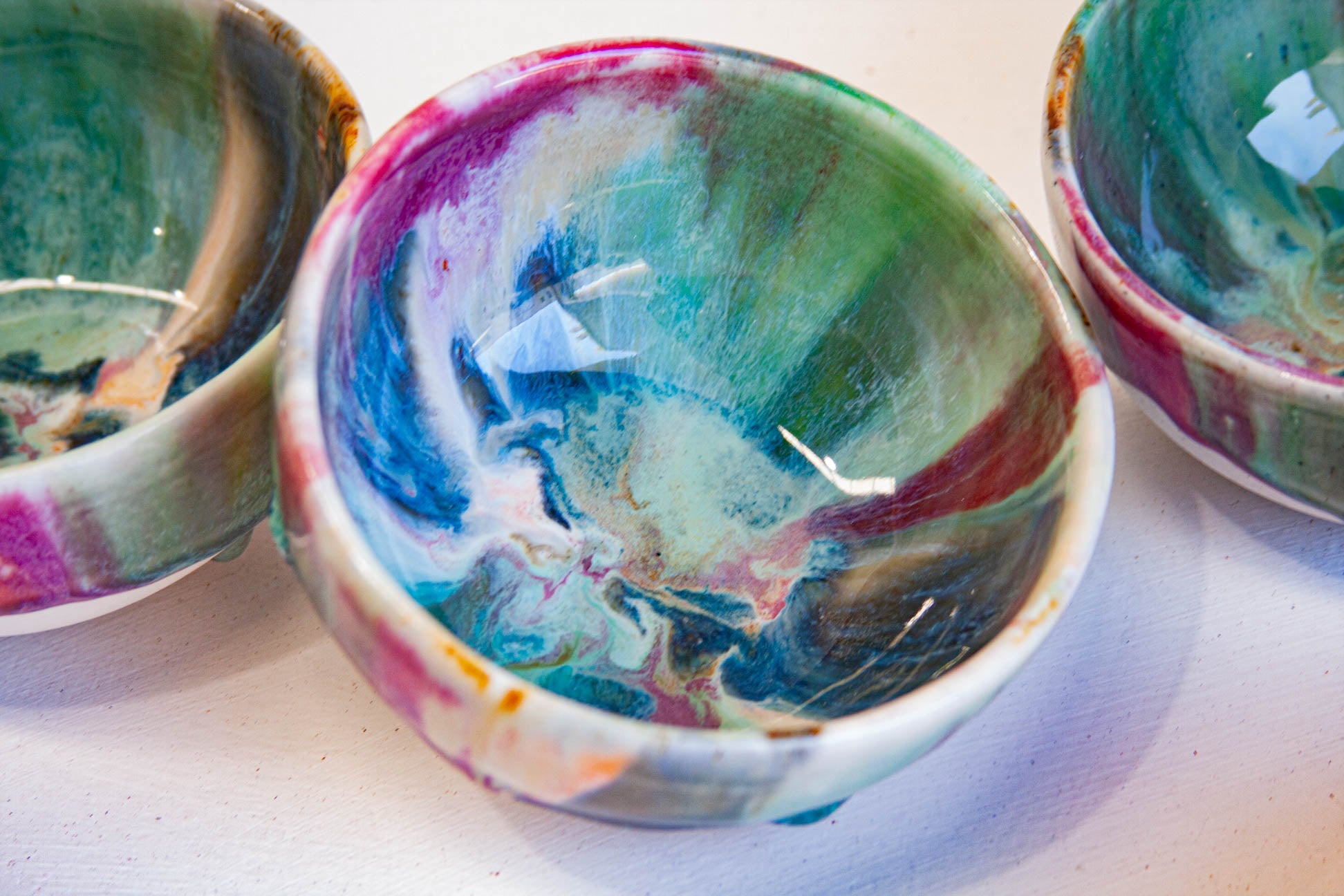 Three hand-painted ceramic bowls with a colorful marbled pattern of green, blue, pink, and white, shown on a white surface.