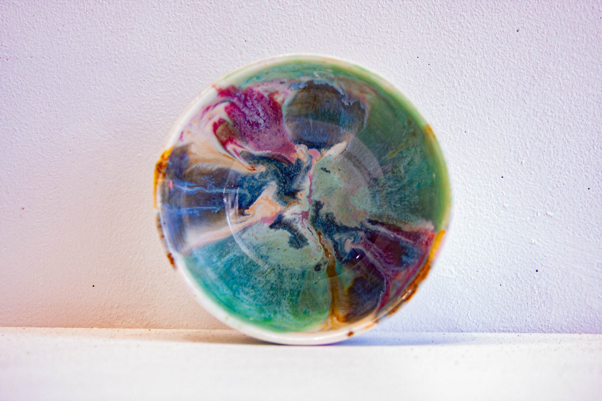 A round ceramic plate with a marbled abstract pattern in teal, green, purple, and white, photographed against a plain light background.