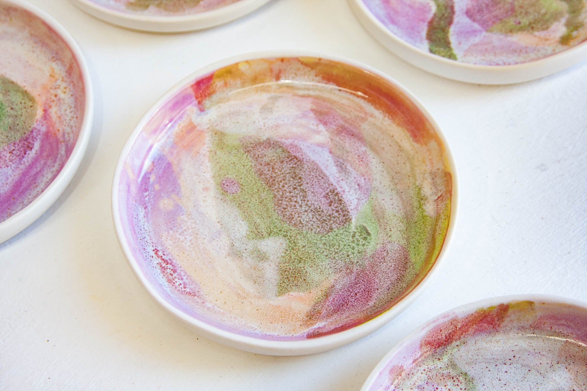 A close-up of a round white ceramic dish with a colorful marbled pattern inside, surrounded by other similar dishes on a white surface.