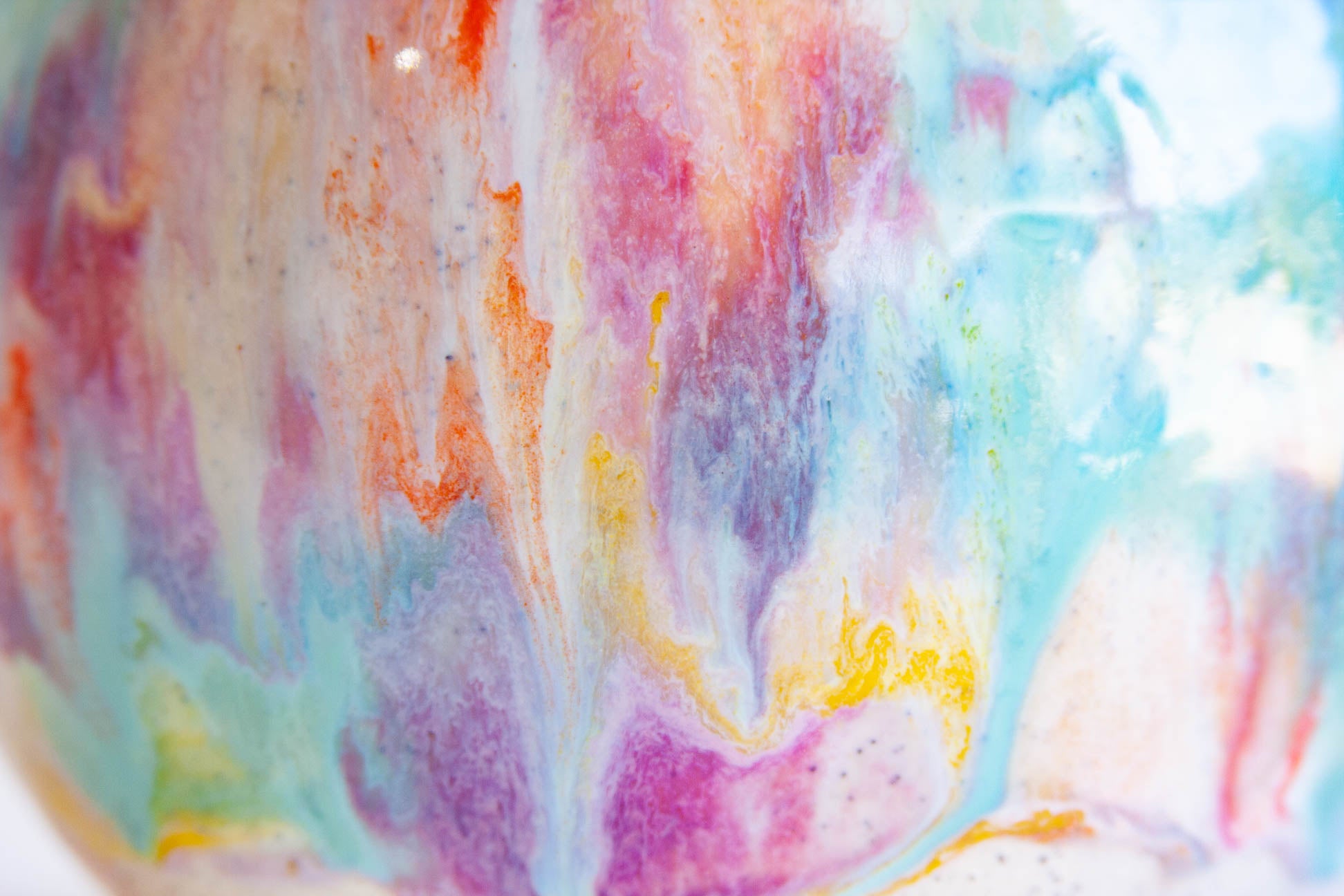 Close-up of a glossy ceramic surface with a marbled abstract pattern in pastel pink, purple, blue, orange, and white.