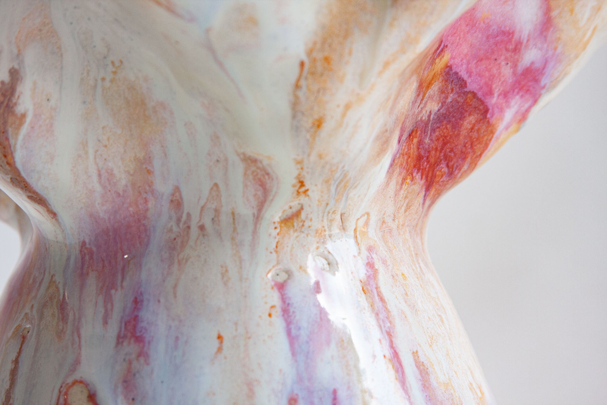 Close-up of a glossy ceramic sculpture or vase with a marbled, fluid art pattern in white, pink, orange, and purple on a light gray background.