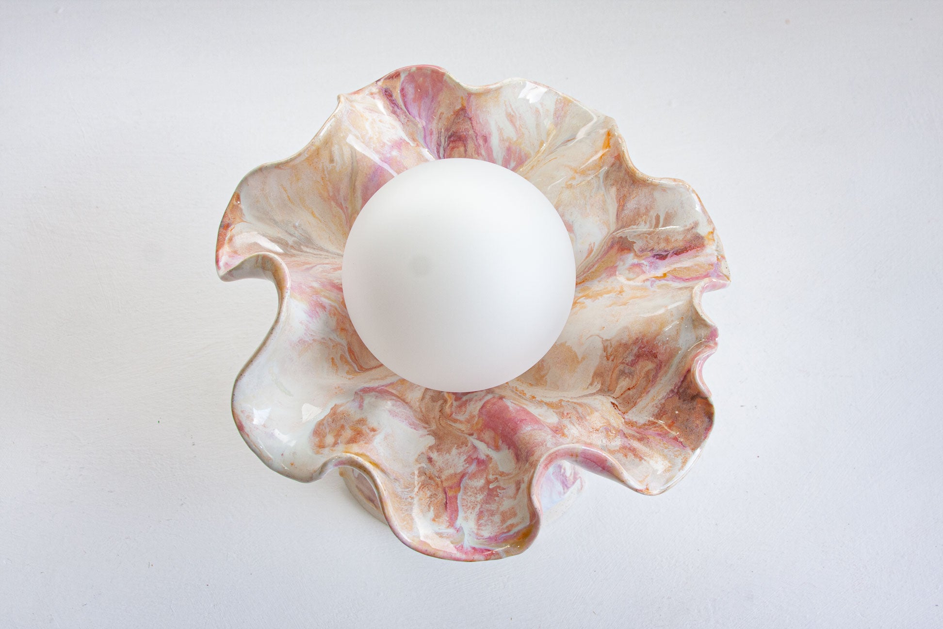 A white spherical object centered inside a scalloped, ruffled dish with a pink, white, and gold marbled pattern, set against a plain white background.