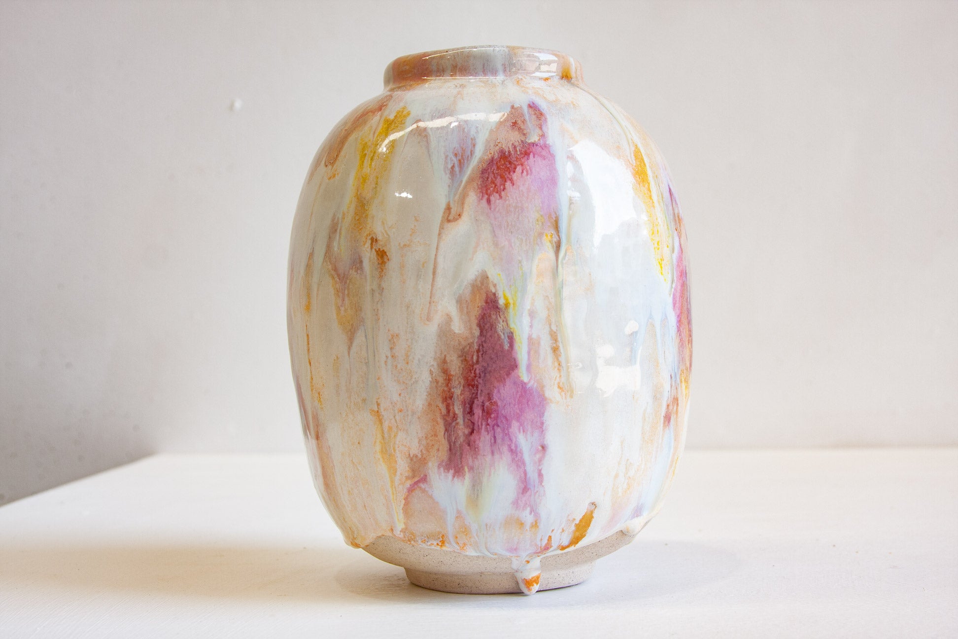 A handmade ceramic vase with a glossy finish, featuring a marbled pattern of white, pink, purple, and gold swirls, displayed on a white surface against a neutral light gray background.