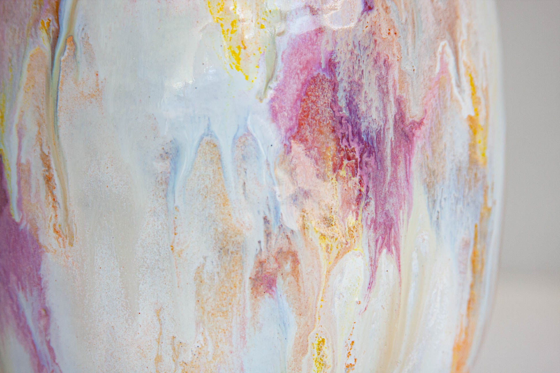 Close-up of a glossy ceramic vase featuring a marbled pattern of white, pink, purple, and gold liquid swirls.
