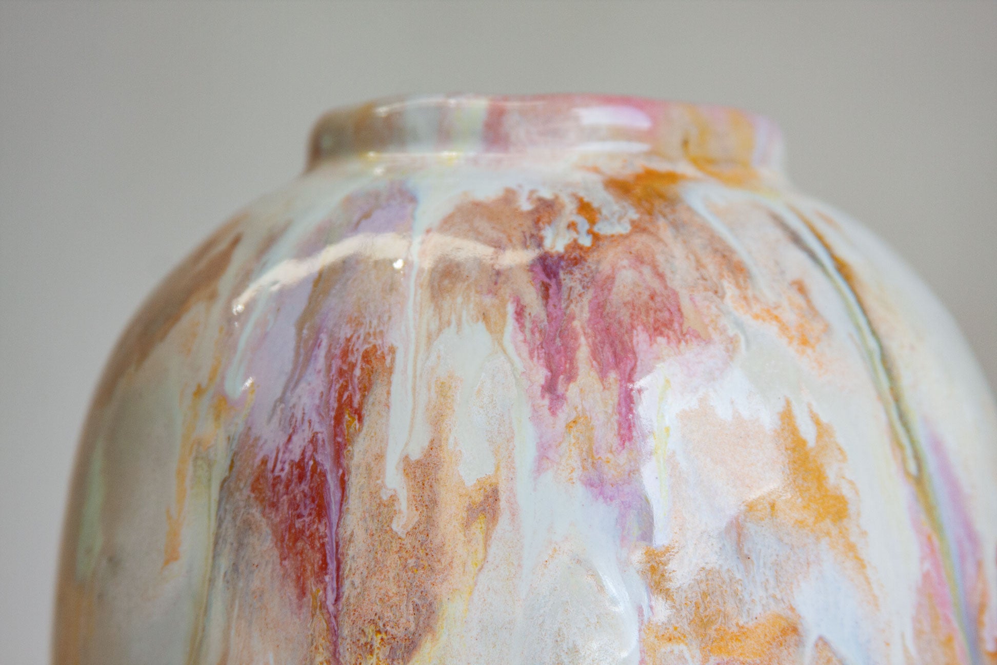 Close-up of a glossy ceramic vase with a marbled, swirled glaze in white, pink, orange, and brown tones against a neutral gray background.