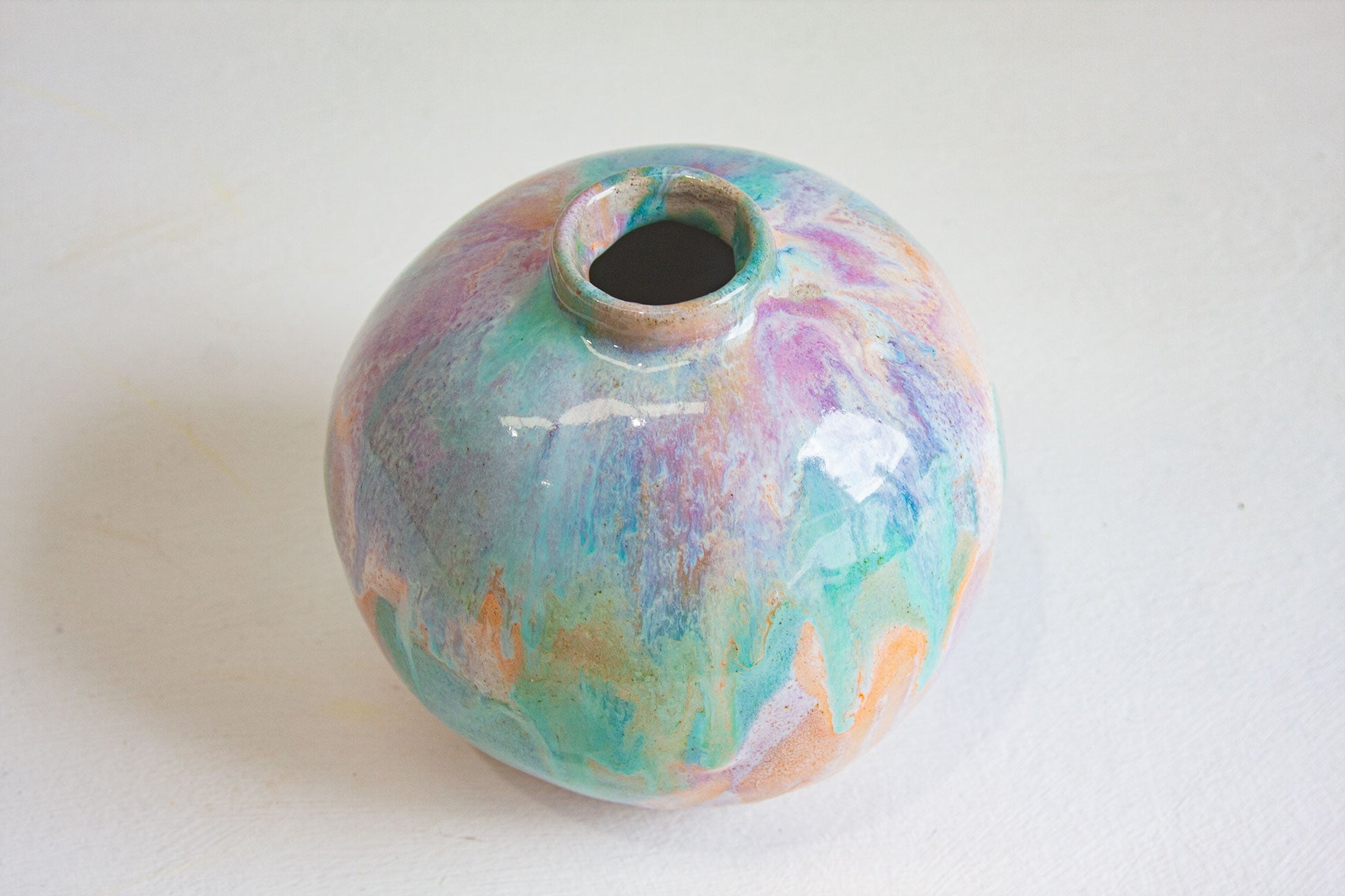Looking down onto a round handmade ceramic vase, showing the small neck opening and the pastel purple, peach and green glaze across the top.