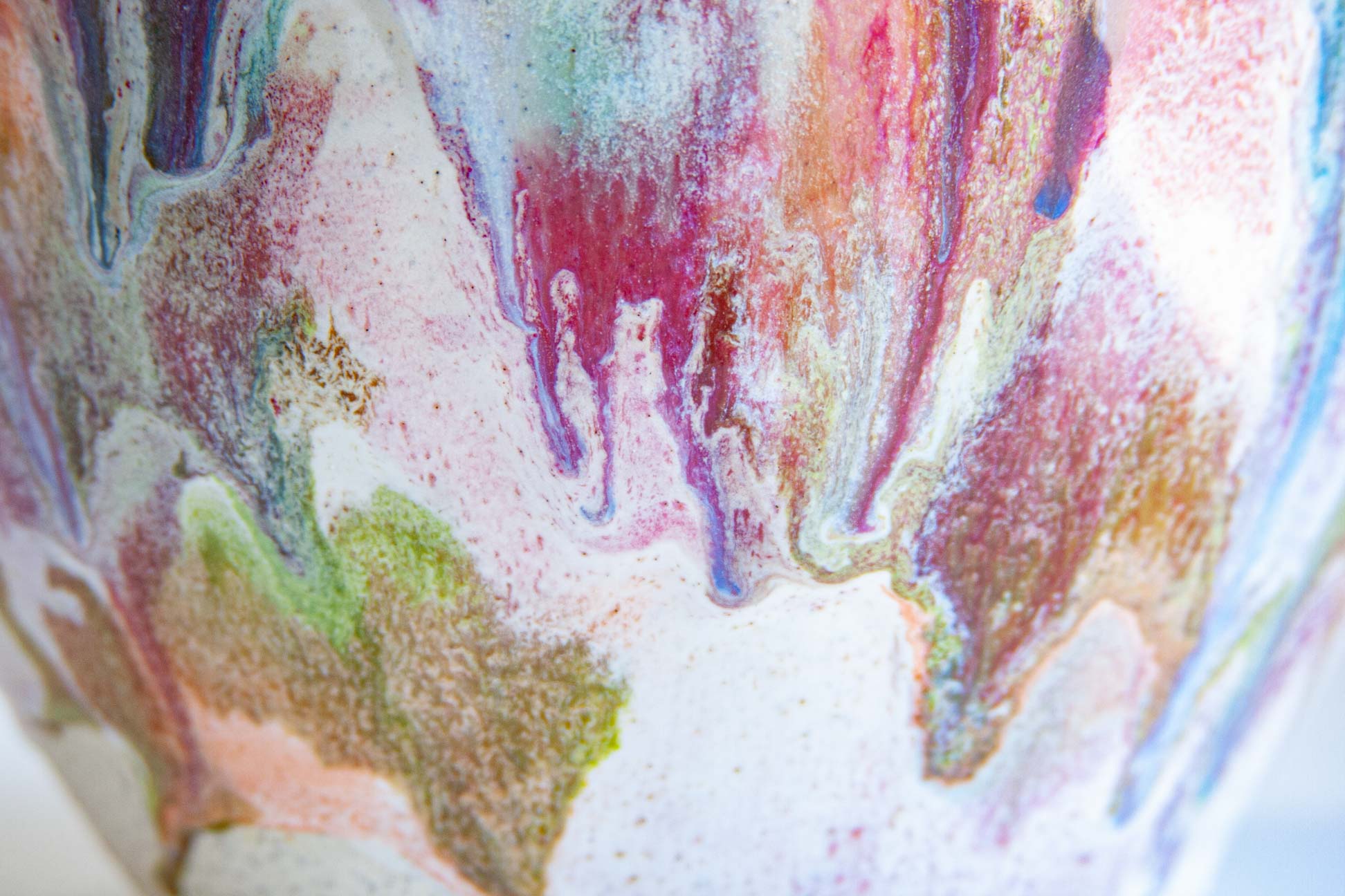 Close-up of a ceramic vase featuring an abstract, marbled glaze pattern with flowing drips of pink, purple, blue, green, and gold on a white base.