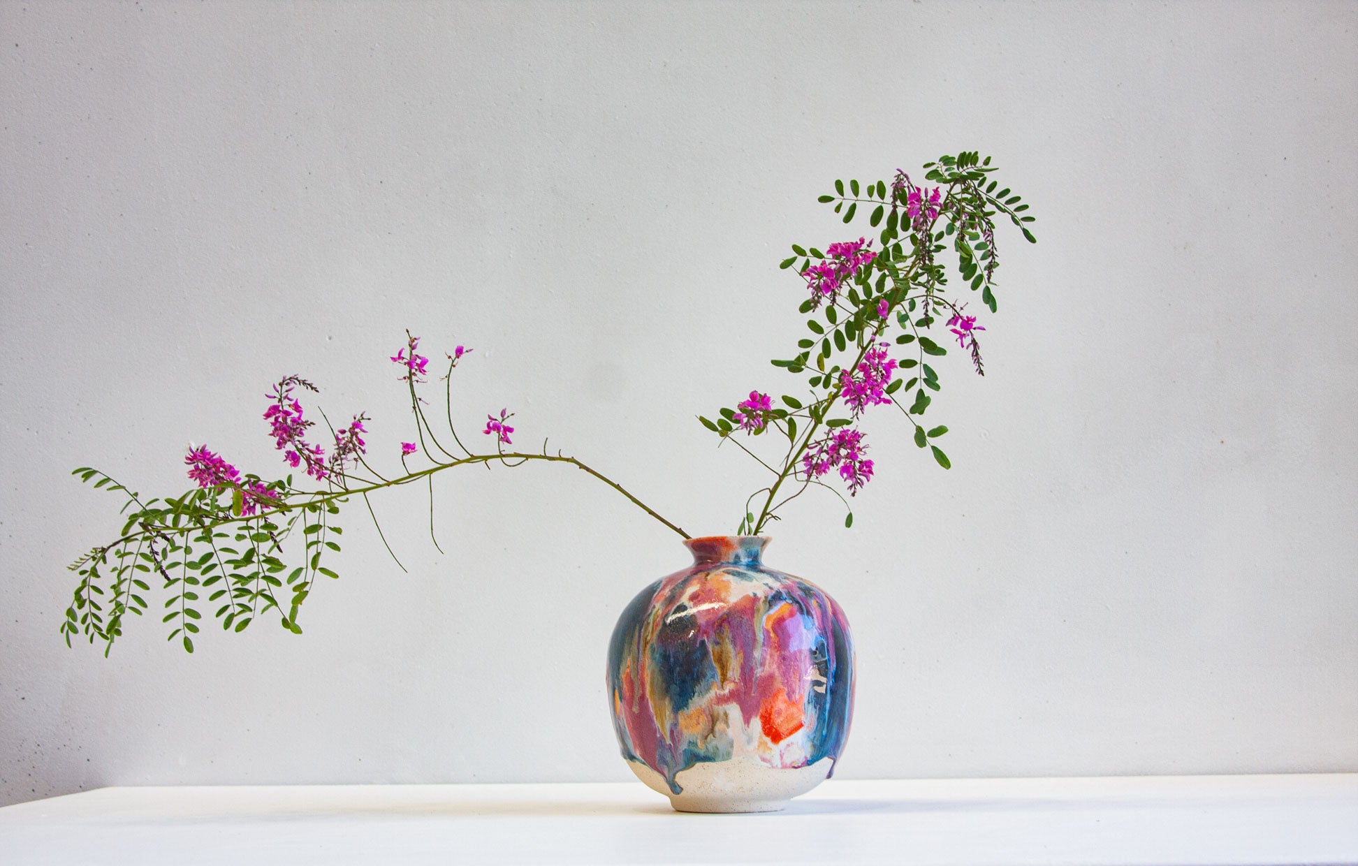 A colorful hand-painted ceramic vase with pink and purple flowers and green leaves, set against a plain light gray background.