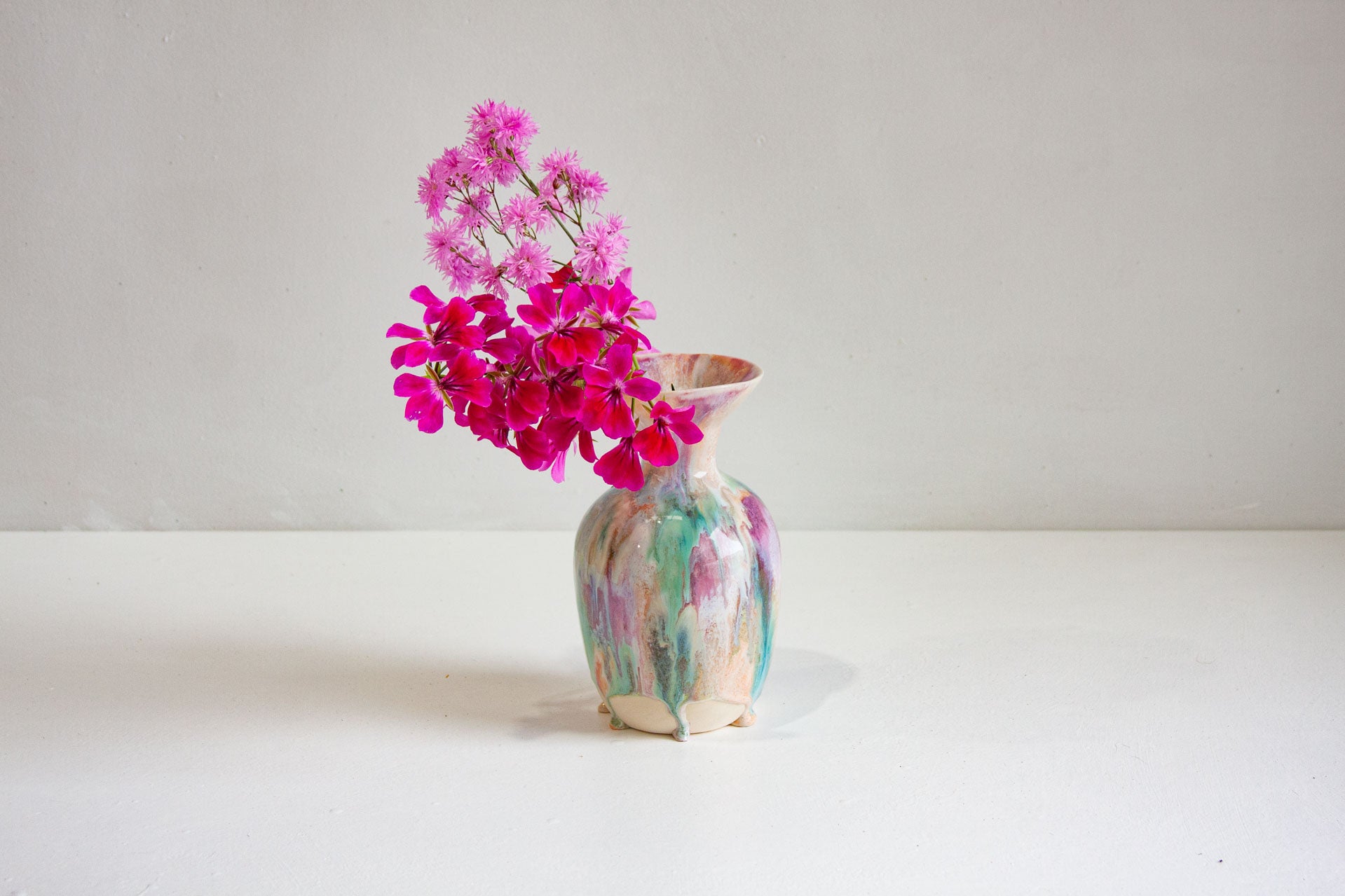 Colorful vase with pink flowers on a white surface and background