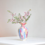 Multicolored vase with flowers on a white surface against a plain wall.