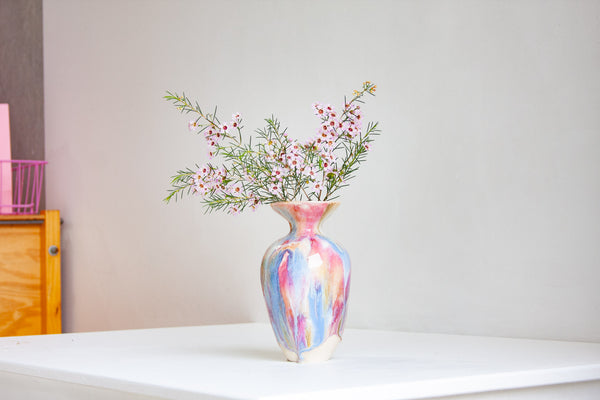 Multicolored vase with flowers on a white surface against a plain wall.