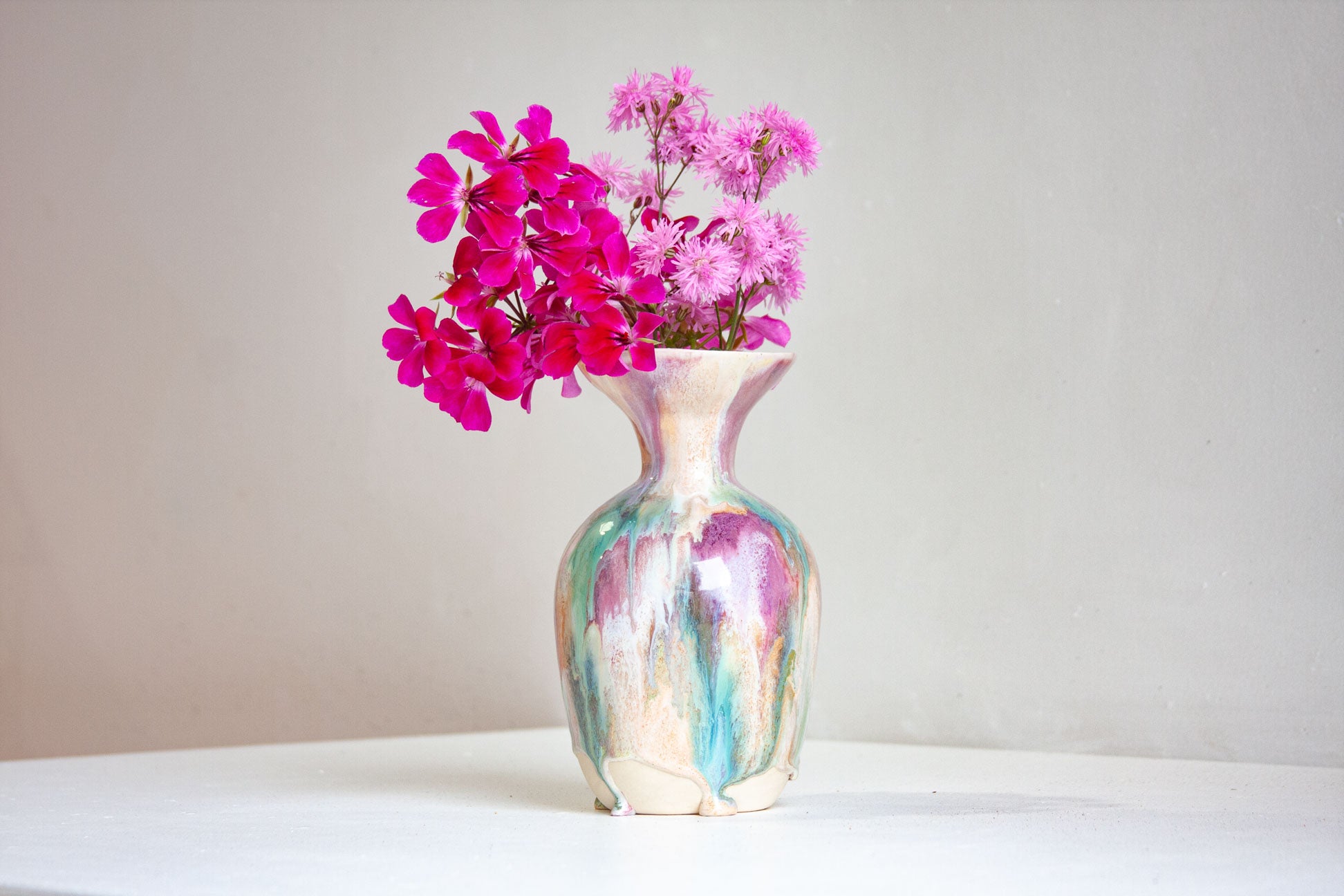 Vase with pink flowers on a white surface and light gray background