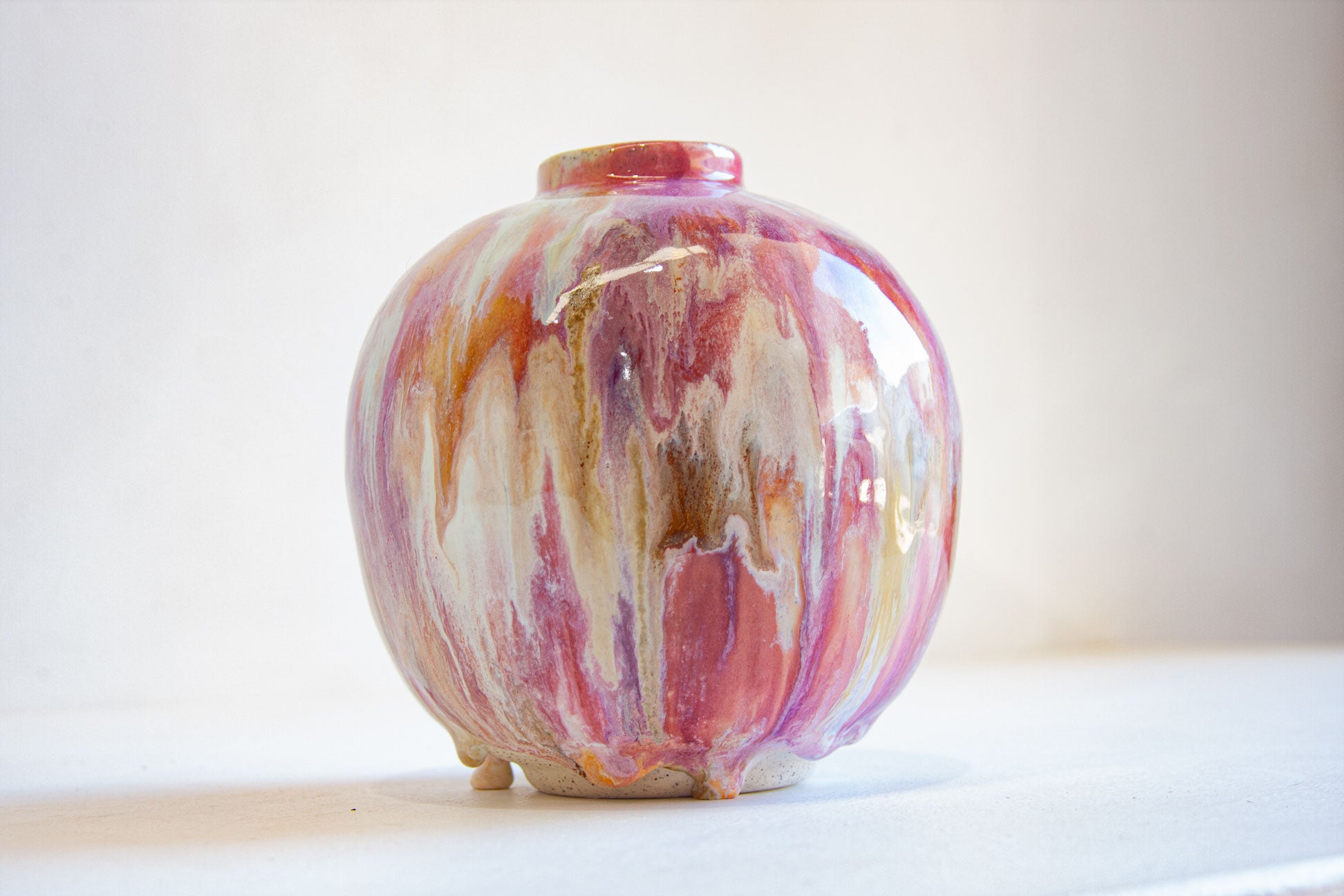 A small round ceramic vase with a glossy finish, featuring a marbled swirl pattern of pink, purple, brown, and cream, set against a plain light background.