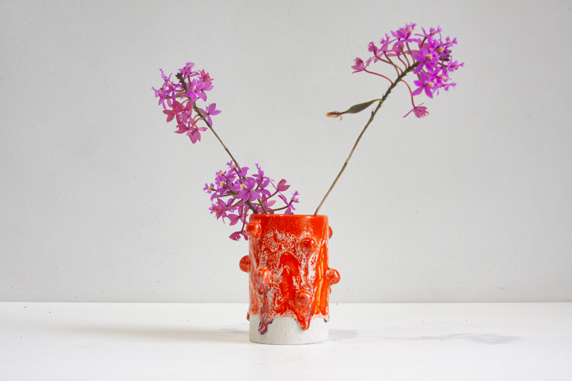 handmade ceramic small cylinder vase with little clay baubles attached to the body of the vase, glazed in orange, white and pink.