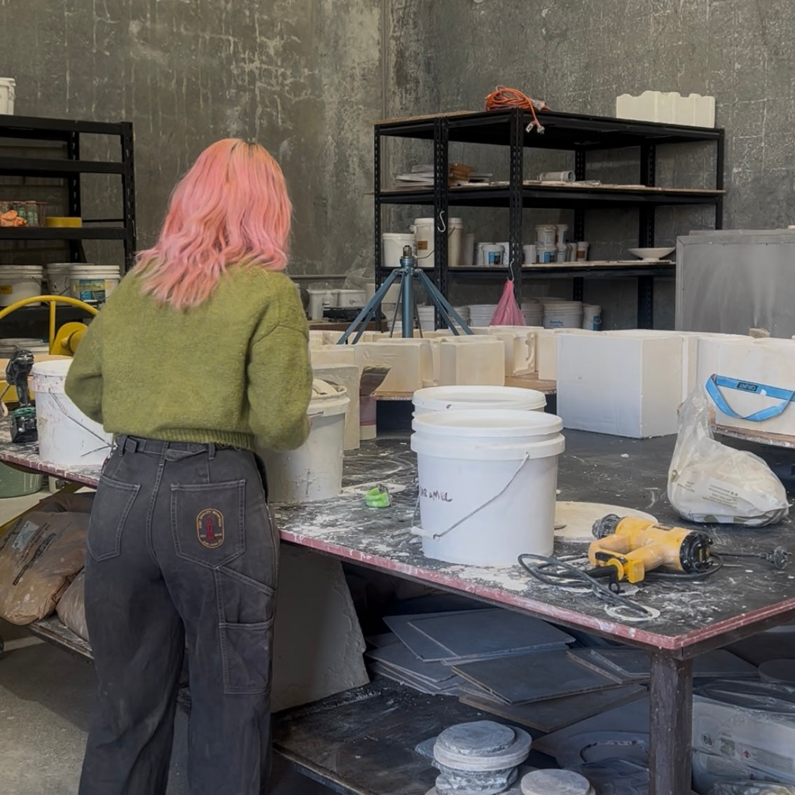 Rhiannon Gill at the bench in her Bellambi studio, working on slip cast pieces beside plaster moulds