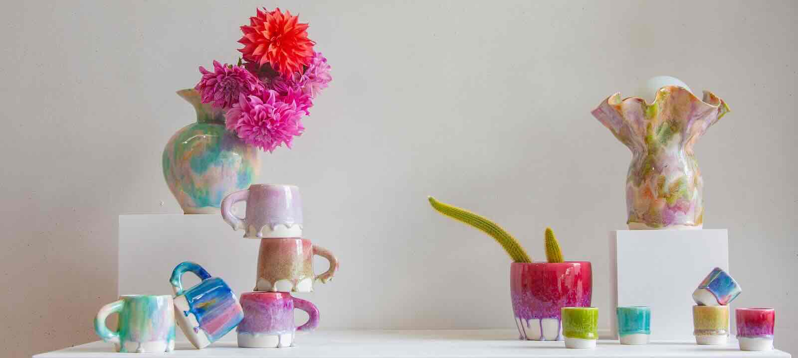 colourful handmade ceramic vases, table lamps, mugs and planters arranged on a table with plinths